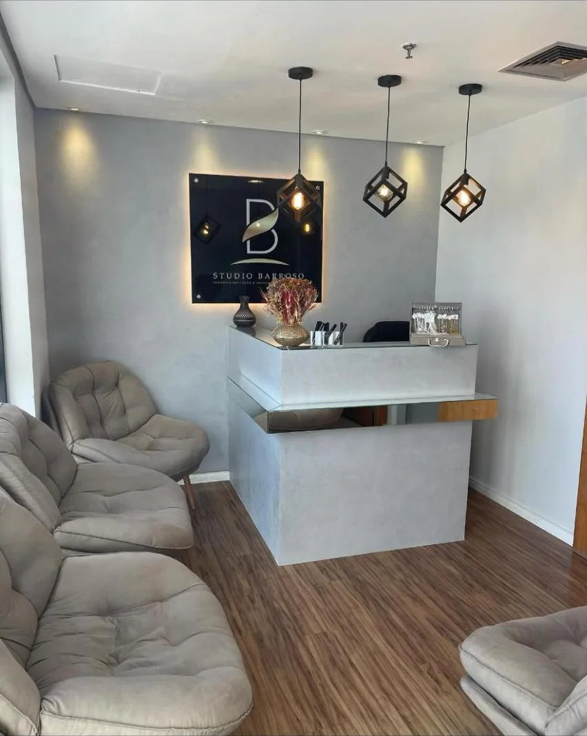Recepção do Studio Barroso com placa preta iluminada com o logo B, pendentes pretos e poltronas cinza